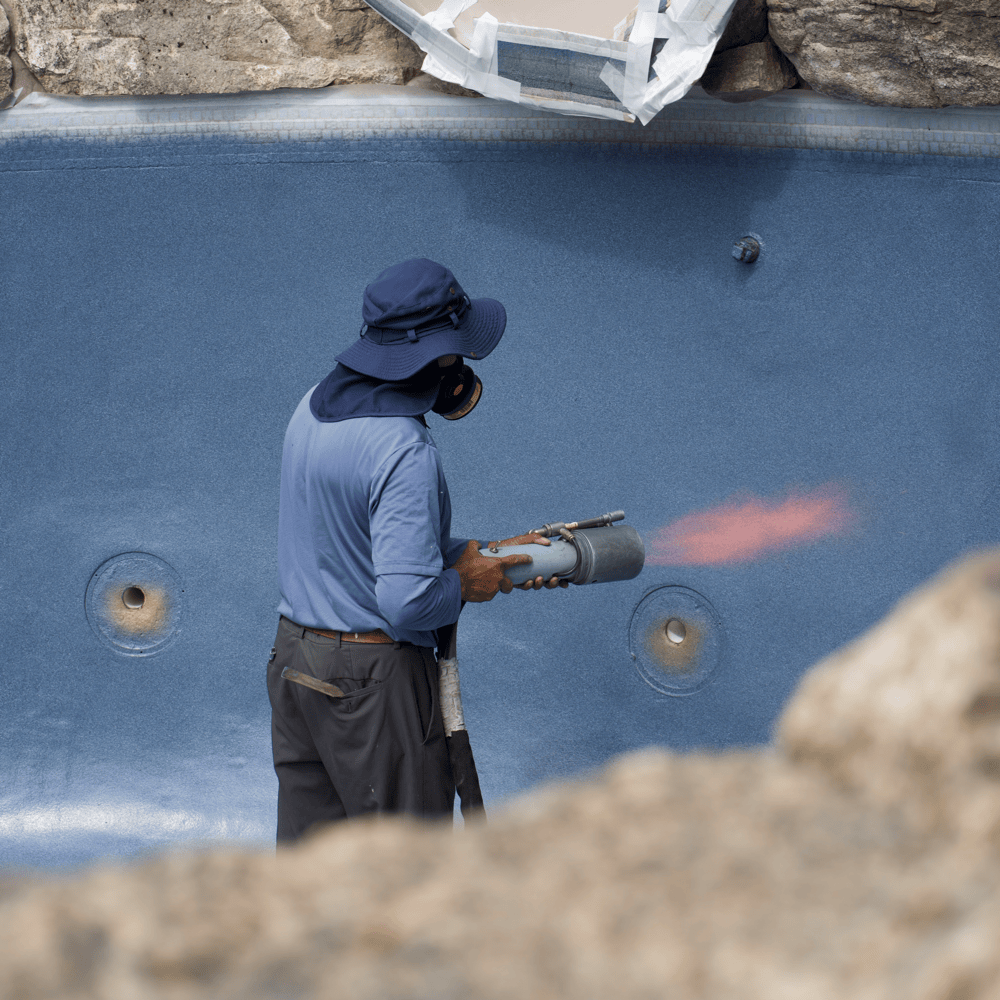 A close-up view of a worker applying ecoFINISH coating to a pool. The worker is using tools to carefully coat the pool's surface with ecoFINISH, ensuring even application.