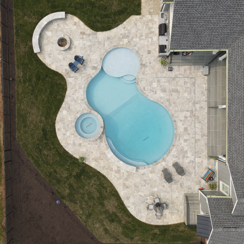 A bird's-eye view of an ingound ecoFINISH-coated pool coated with blue mist, showcasing the smooth and reflective surface of the pool. The view includes the surrounding deck area.