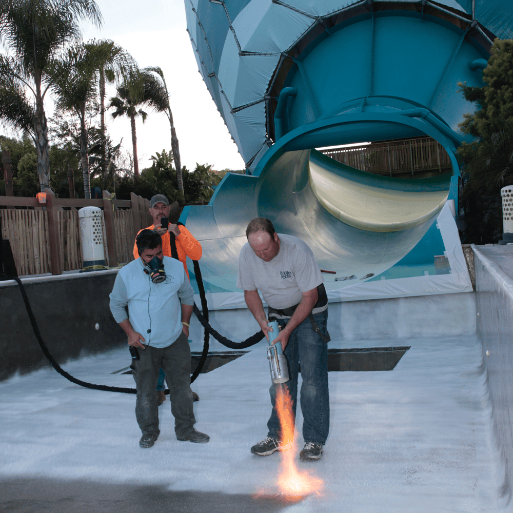 Workers coating a commercial pool with ecoFINISH at the base of a large slide. The workers are applying the ecoFINISH coating to ensure even coverage.