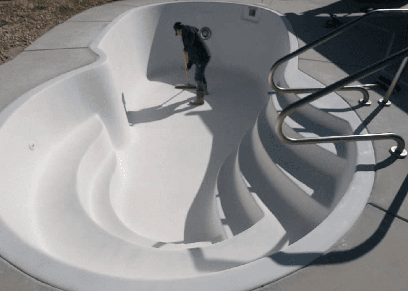 A person cleaning an empty in-ground pool seen from a higher angle.