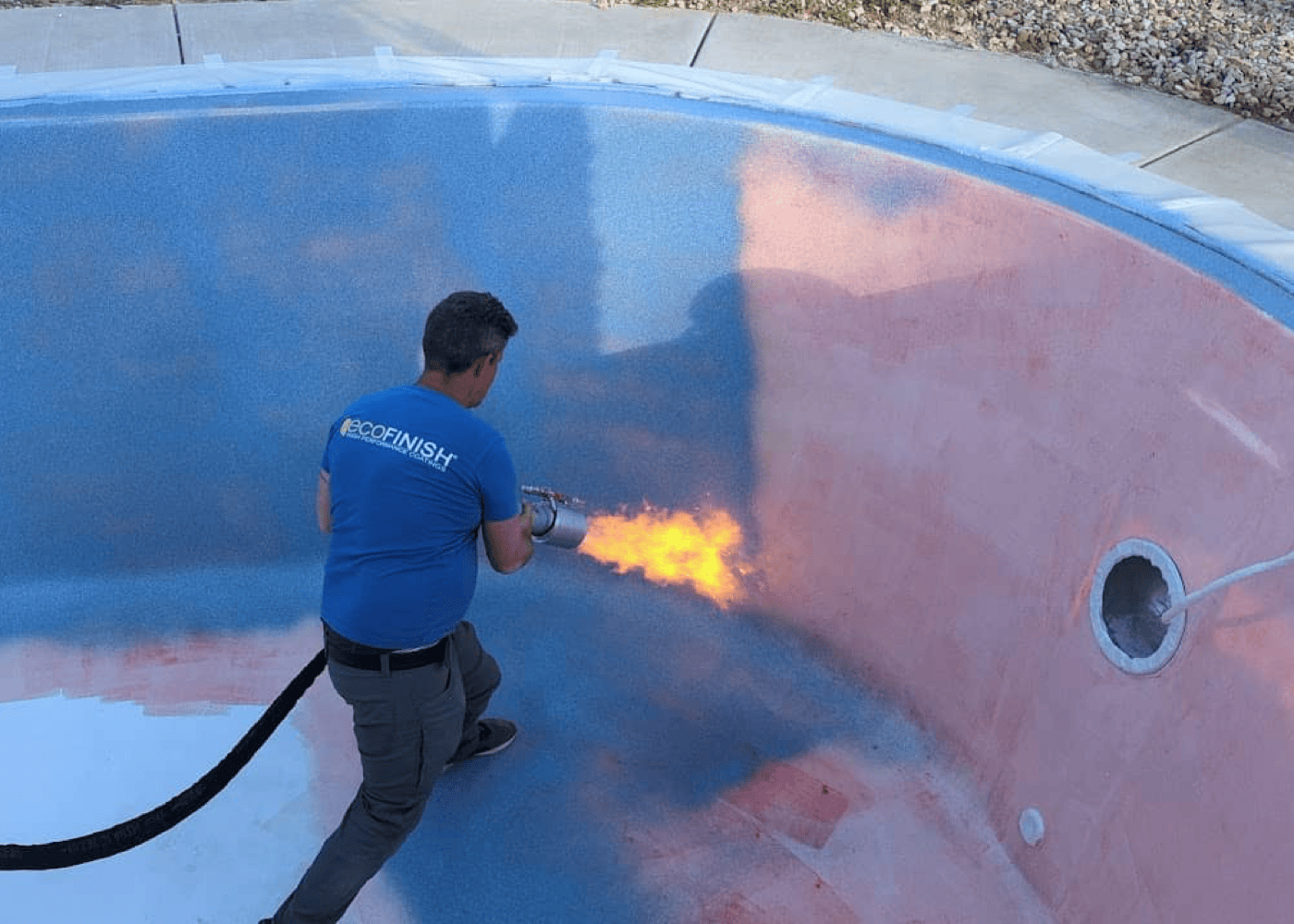 An empty in-ground pool in the process of being coated with the first layer of ecoFINISH. Worker is applying the coating material to the pool's interior surface.