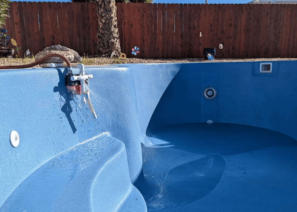 A residential hot tub with a bright blue, textured interior. It is being filled with water from a hose. The hot tub has built-in stairs and seating.
