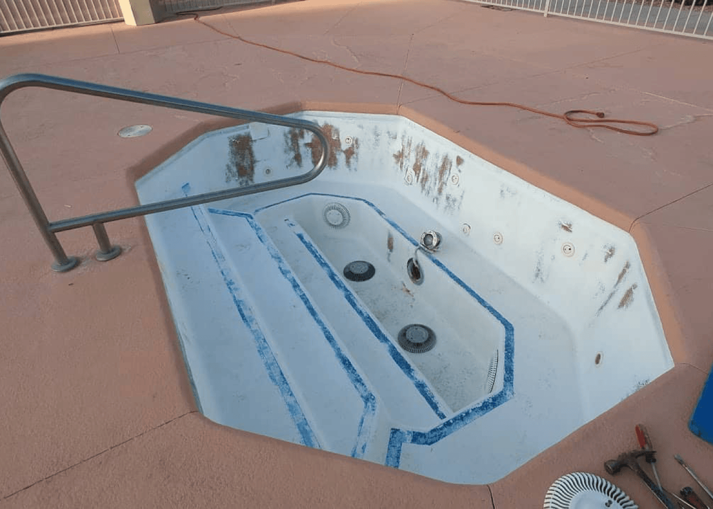 A small, empty in-ground pool showing signs of wear and staining. The pool's surface appears worn down and discolored in areas. In a different angle.