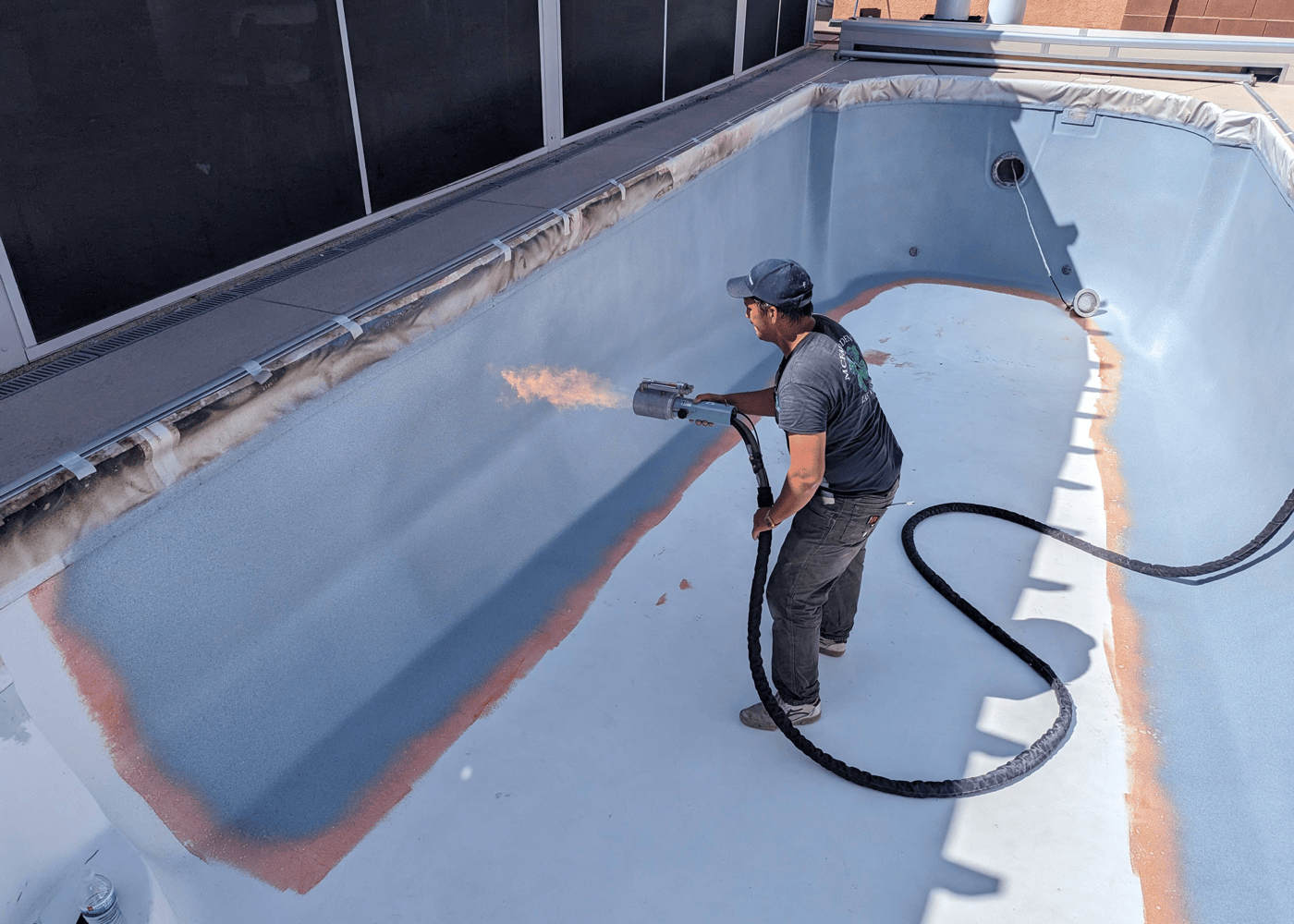 An empty in-ground pool in the process of being coated with ecoFINISH. Workers are applying the coating material to the pool's surface.