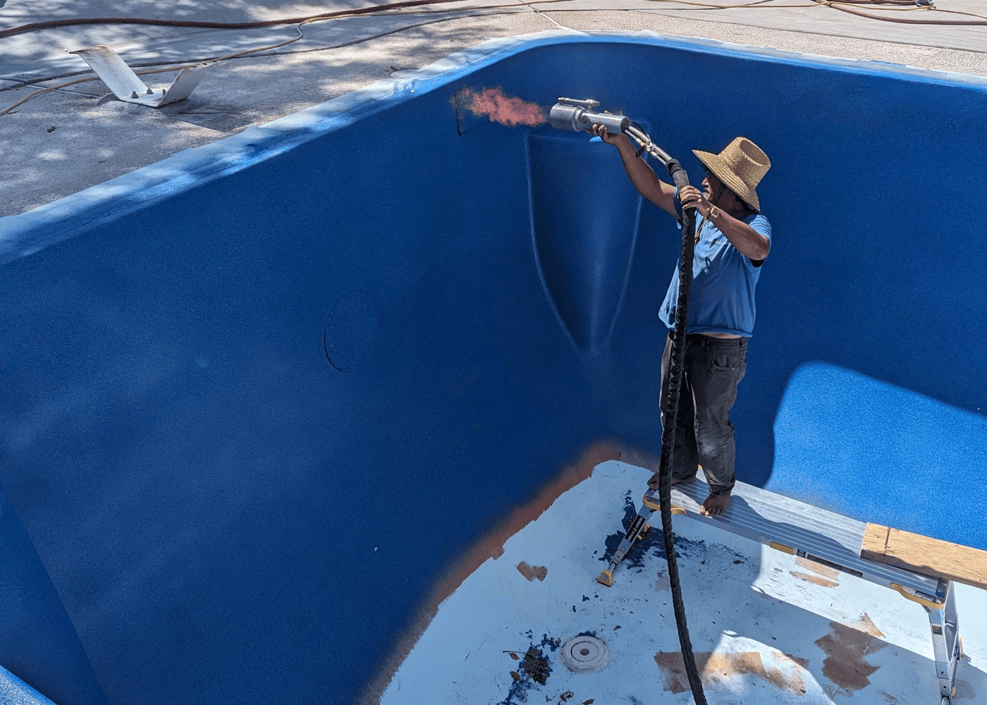 An in-ground fiberglass pool being coated with ecoFINISH polyFIBRO in Pacific Blue. Workers are applying the vibrant blue coating to the pool's surface.