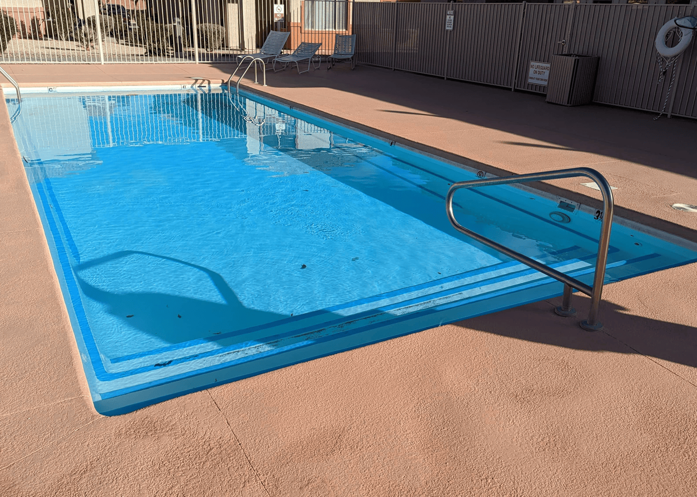 A filled swimming pool viewed from a vertical angle, showcasing its clear blue water reflecting sunlight.